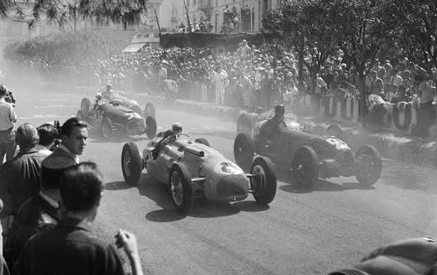 Grand Prix cars streaming past a packed spectator bank at Monaco